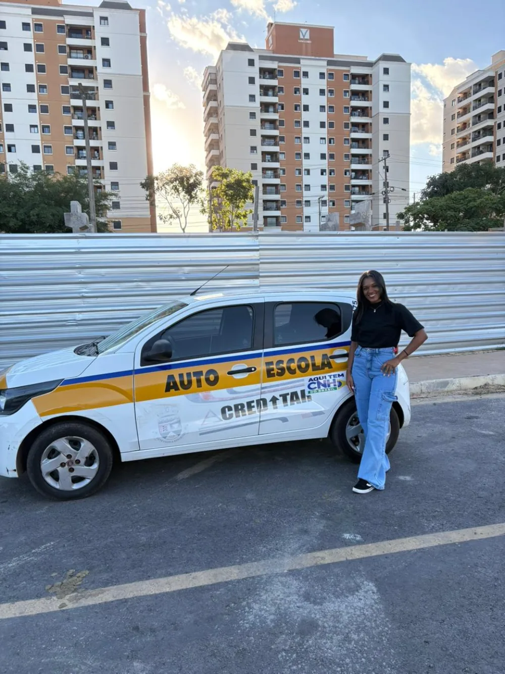 Aluna aprovada ao lado do carro da autoescola após tirar a CNH